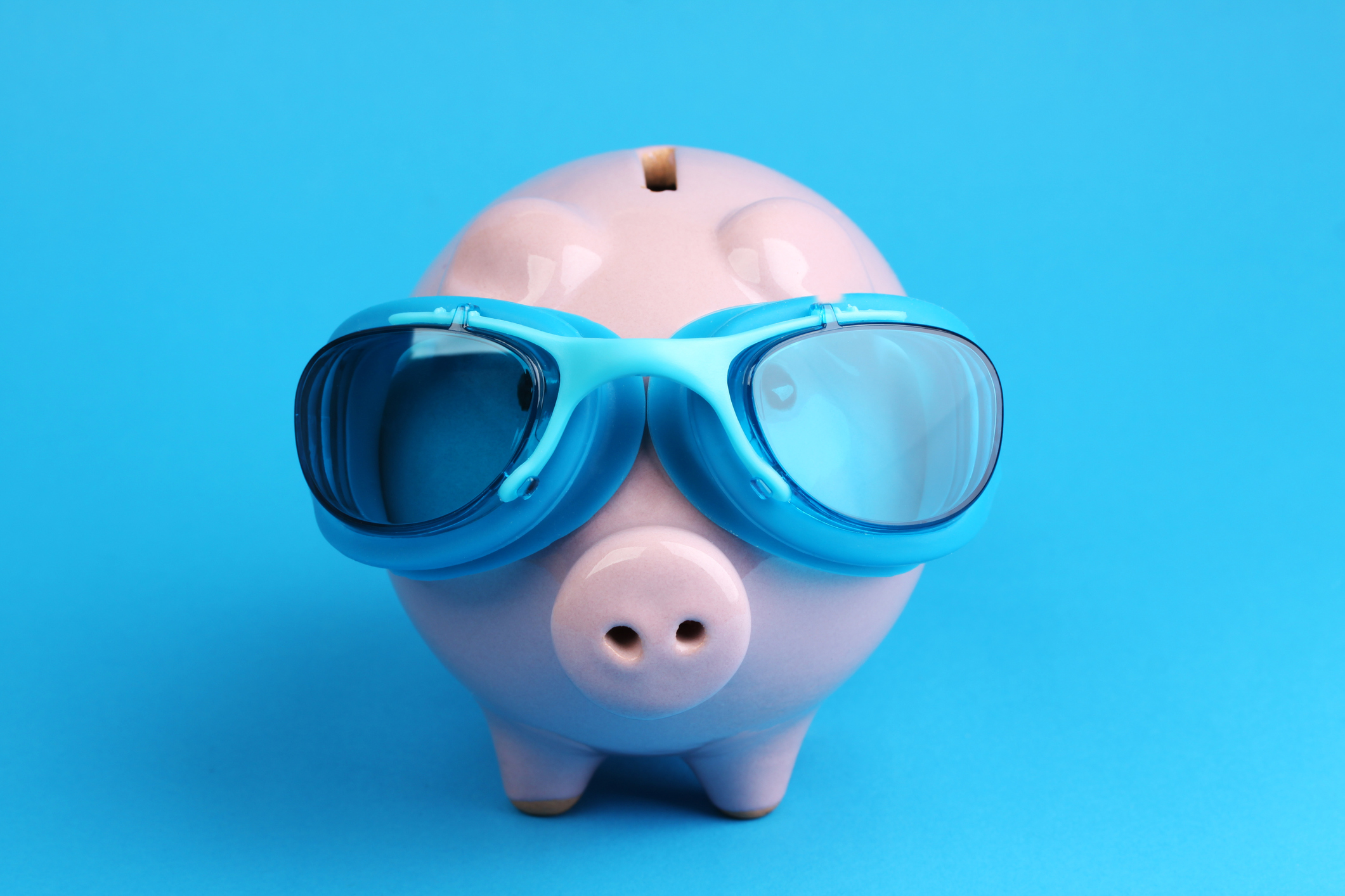 Pink piggy bank with blue swimming goggles on blue background like swimmer