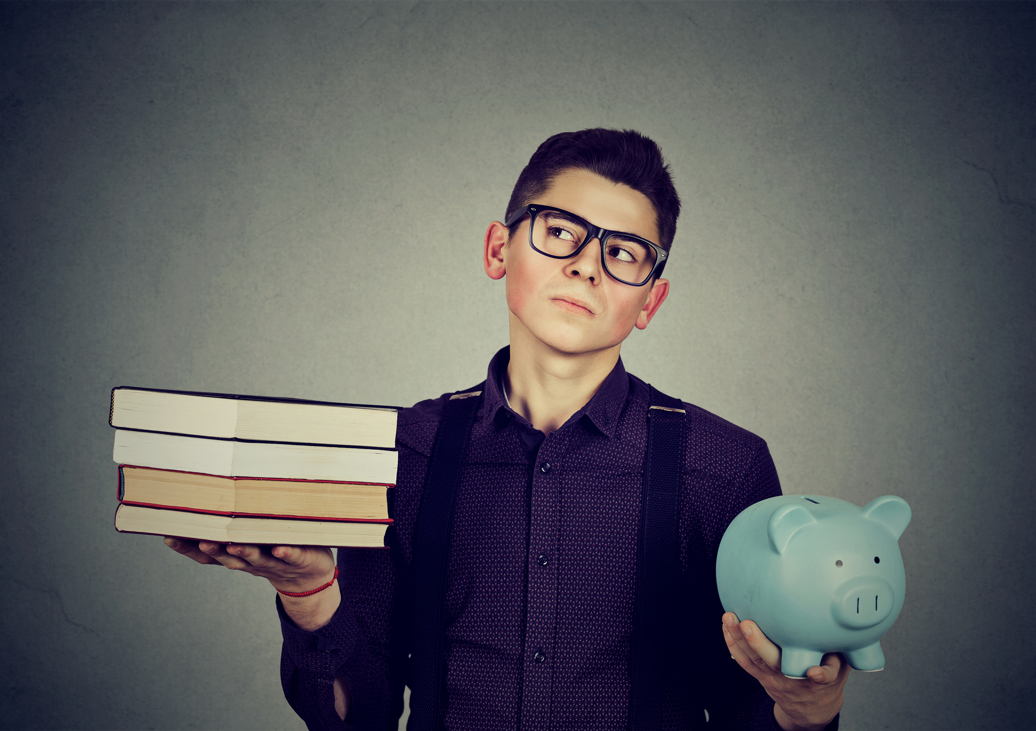 Young man with stack pile of books and piggy bank full of debt