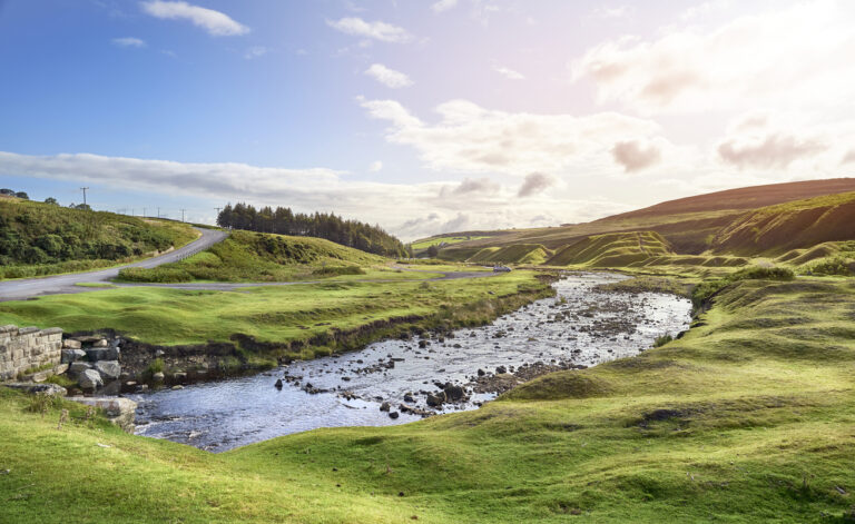 The river, Bolliehope Burn, that runs through the green pastures on the edge of the moors with the disused quarry remains in the distance.