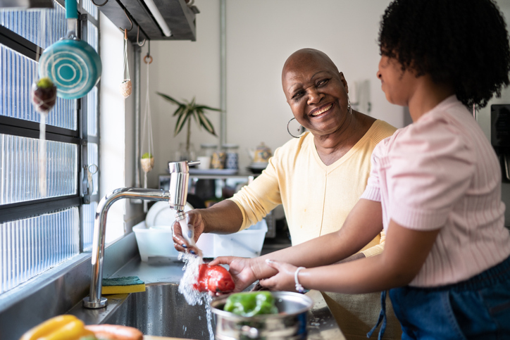 Grandmother and granddaughter washing vegetables together at home