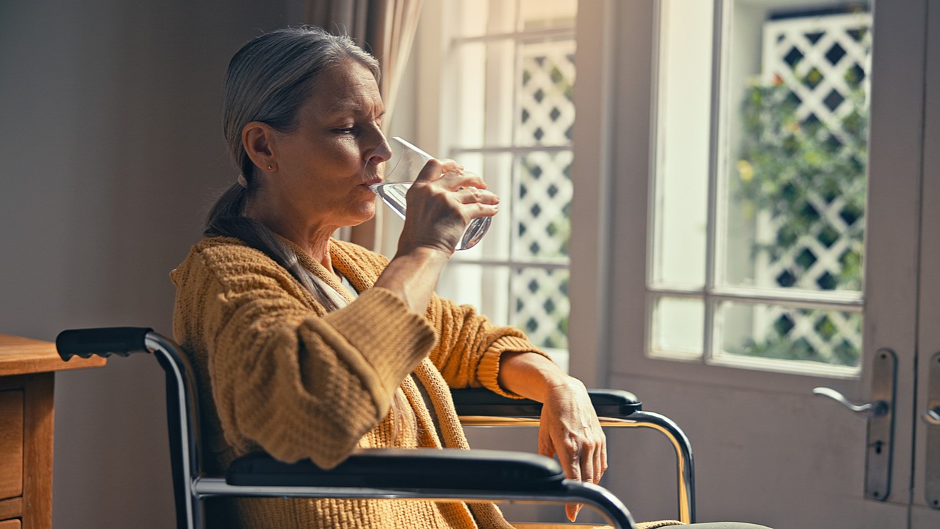 Senior lady in a wheelchair drinking a glass of water