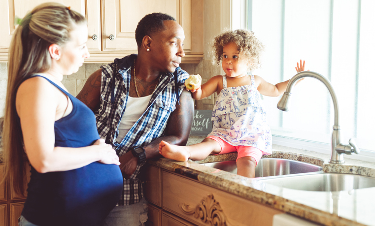 Family at home standing by kitchen sink. Mother is pregnant